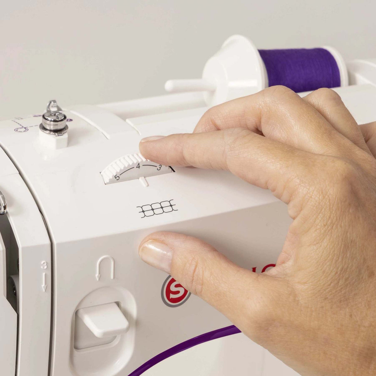 Hand adjusting a dial on top of the Singer M3500 above the reverse lever