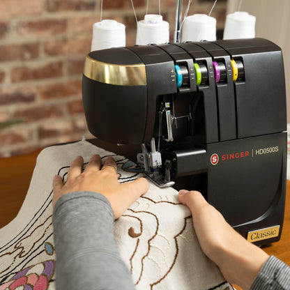 Hands guiding embroidered fabric under the needle of the Singer HD0500S