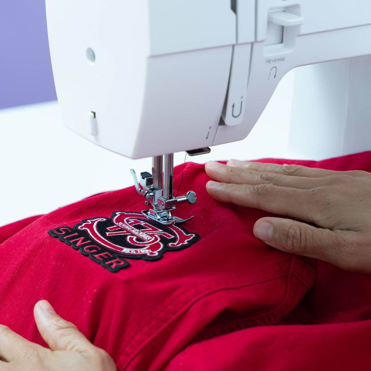 Singer Prisma Heavy Duty presser foot stitching a patch onto red fabric near the reverse lever