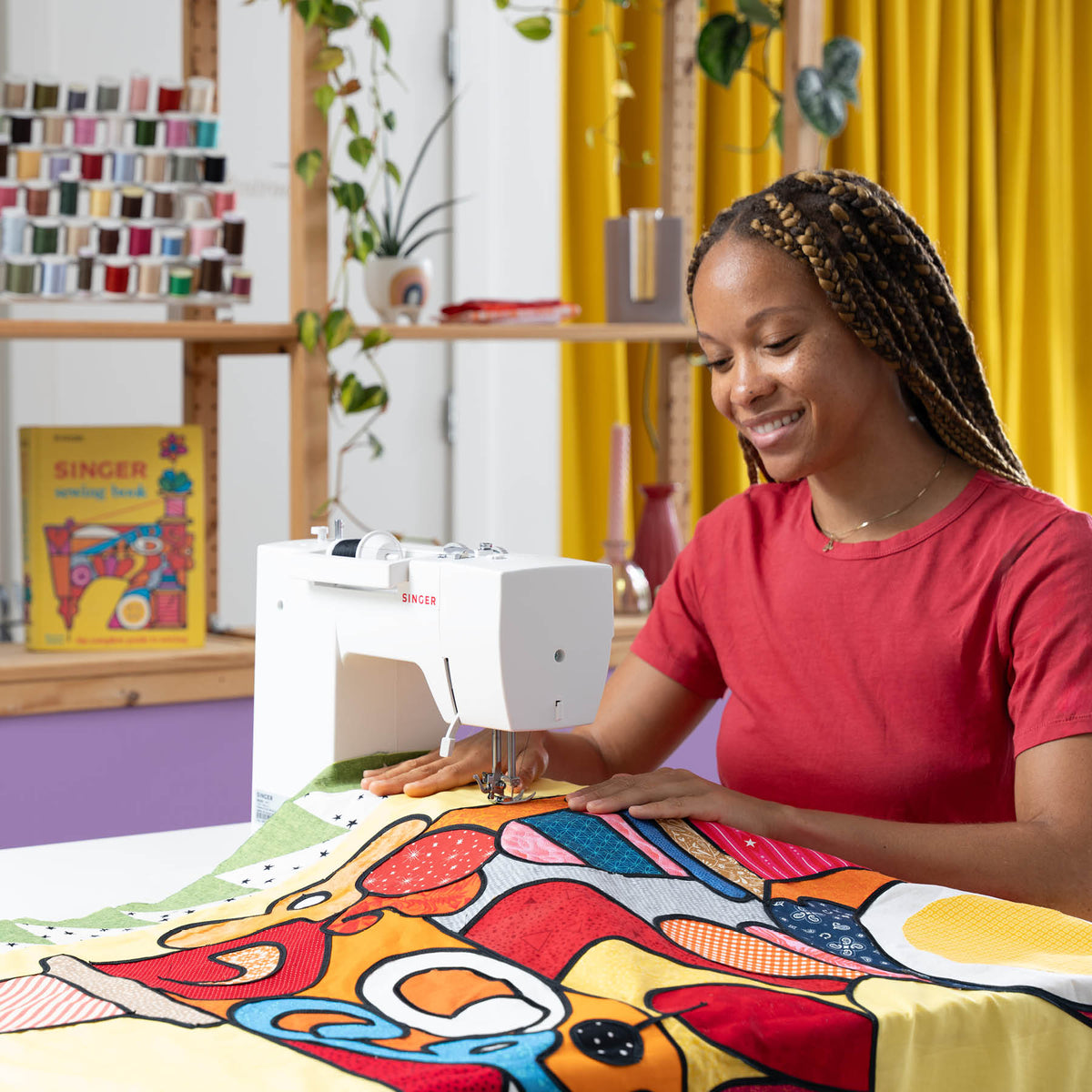 Woman sewing a large colorful quilt top on a Singer Prisma Heavy Duty at a table