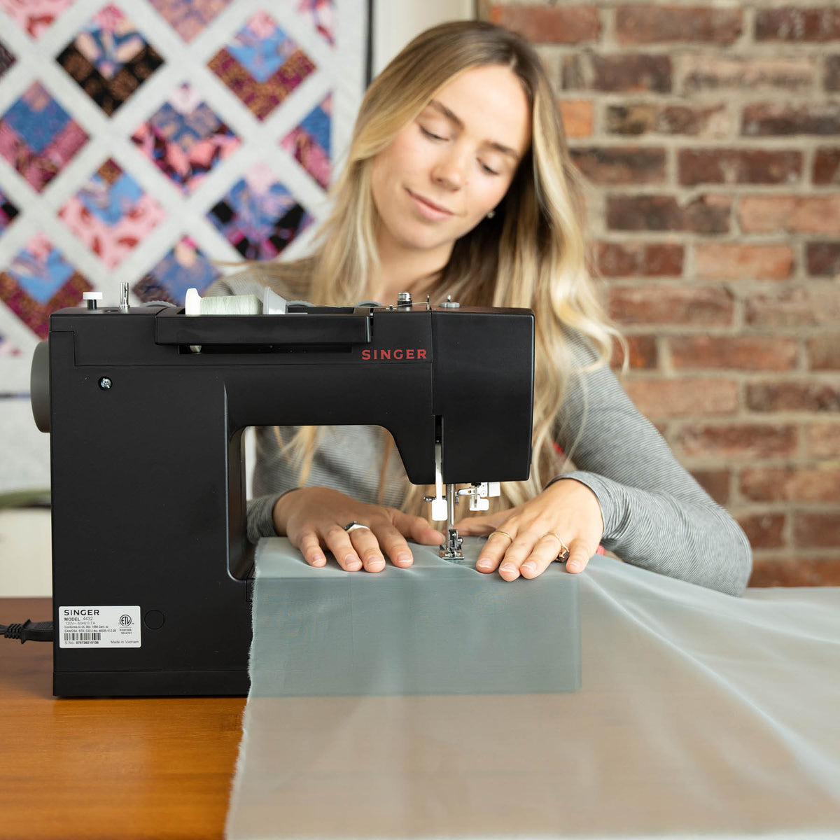 Singer Heavy Duty 4432 Black sewing machine with a seated sewist stitching light gray sheer fabric