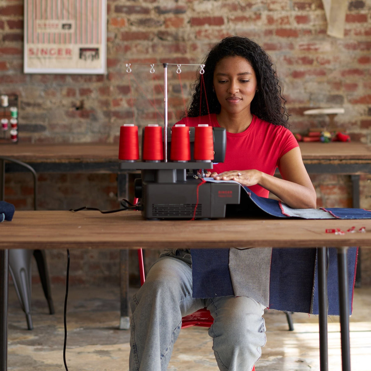 Woman sewing denim on a Singer HD0460 serger at a table with four red thread spools