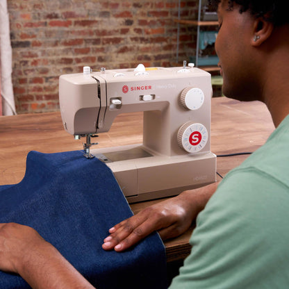 Person sewing blue denim on the Singer Heavy Duty 4523 at a wooden table