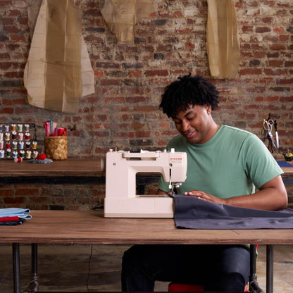 Person sewing gray fabric at a wooden table with the Singer Heavy Duty 4523