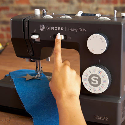 Finger on the speed control slider of the Singer Heavy Duty 4552 Charcoal with denim under the needle