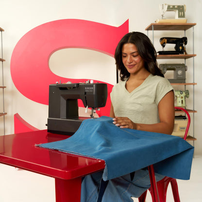 Woman seated at a red table sewing blue fabric on the Singer Heavy Duty 4552