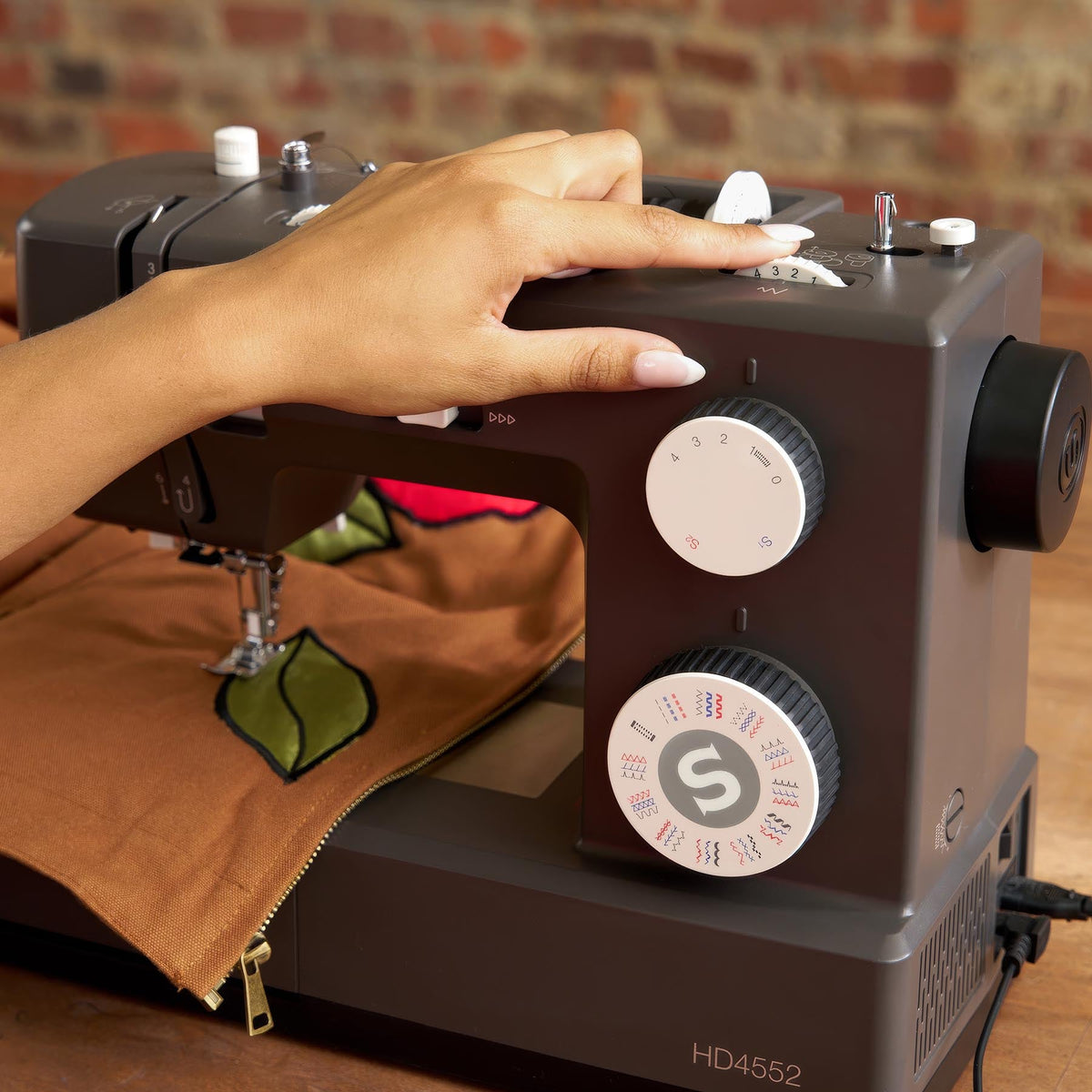 Hand on top of the Singer Heavy Duty 4552 while sewing brown canvas with a green leaf design