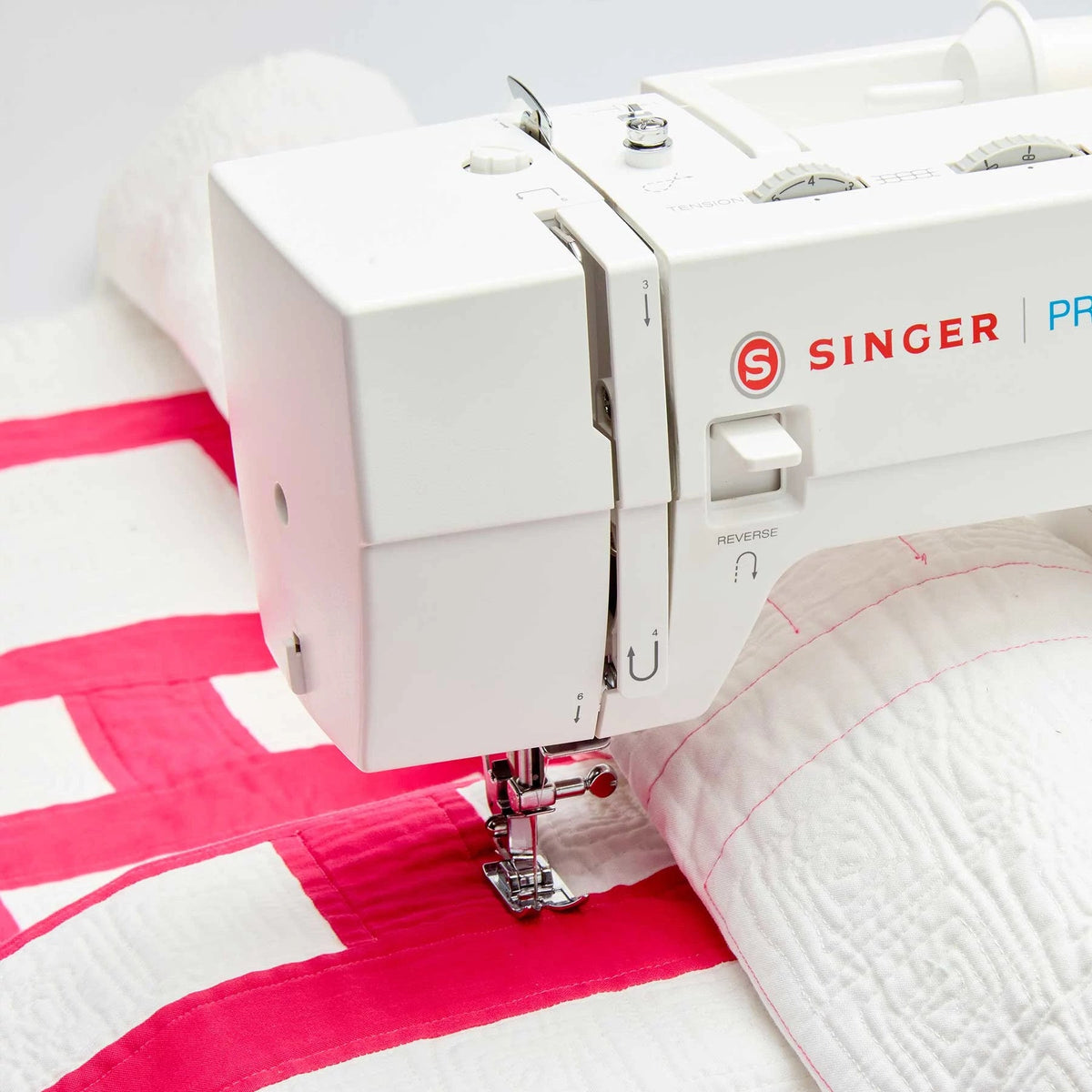 Singer Prisma Heavy Duty presser foot stitching a pink and white quilt near the reverse lever