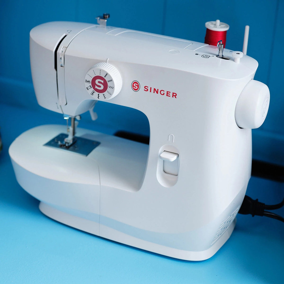 Singer MX60 sewing machine angled view with a spool of red thread on the spool pin