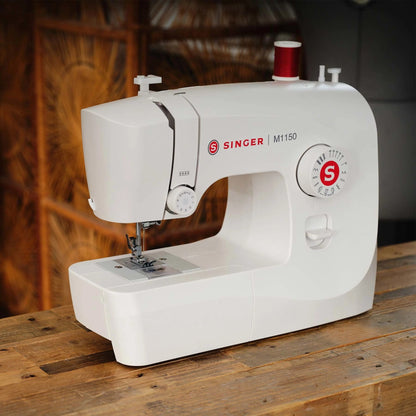 Singer M1150 sewing machine on a wood table with a red thread spool